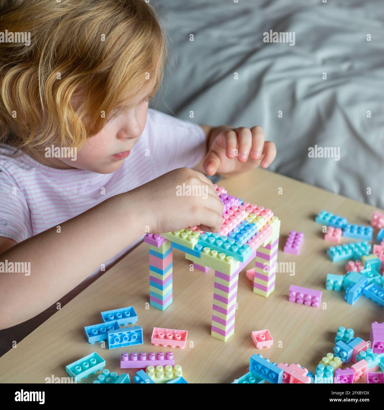 Little beautiful child playing with toy plastic building blocks, sitting at the table. Small girl busy with fun creative leisure activity. Development Stock Photo