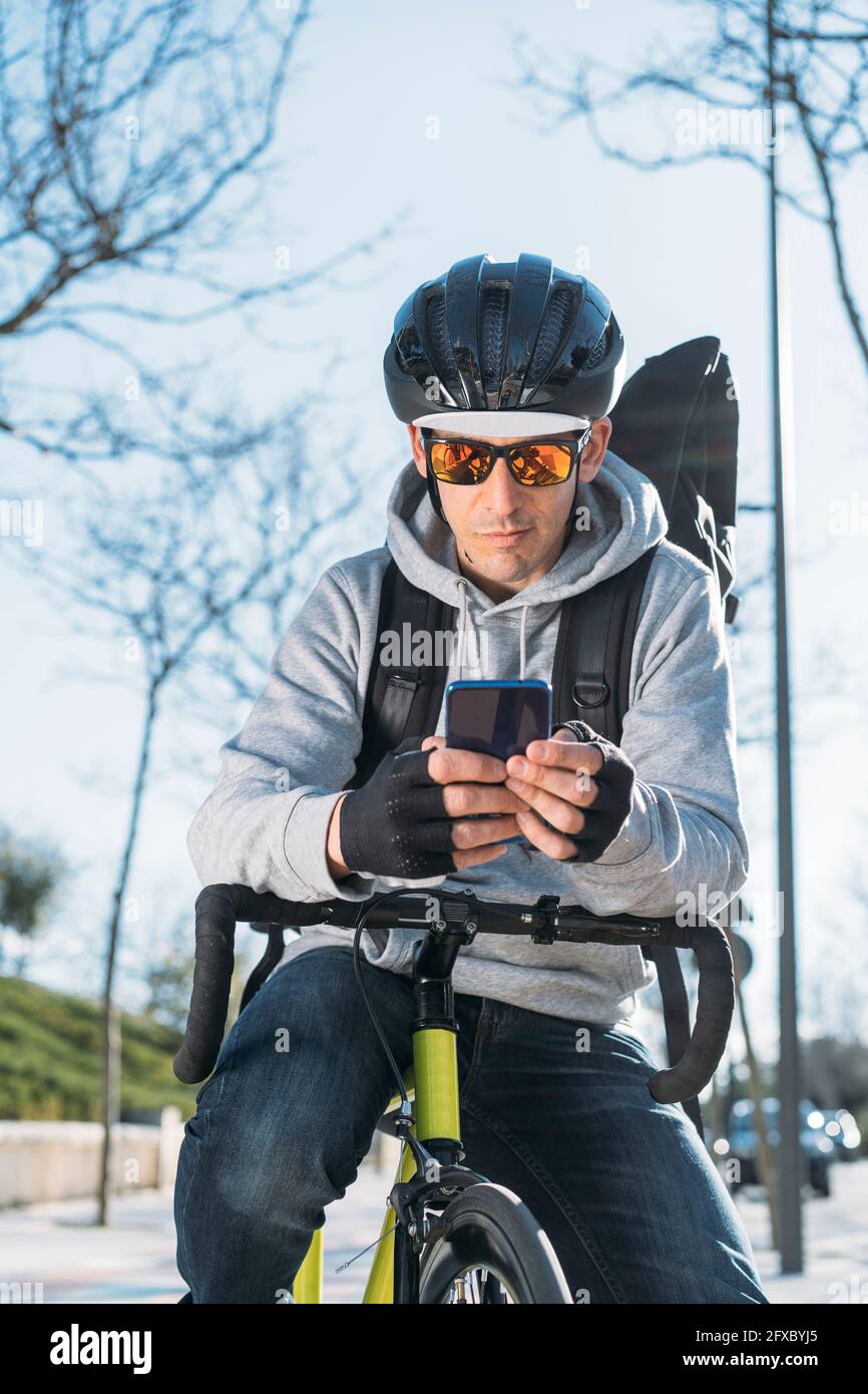 Mature delivery man leaning on bicycle while using smart phone Stock Photo