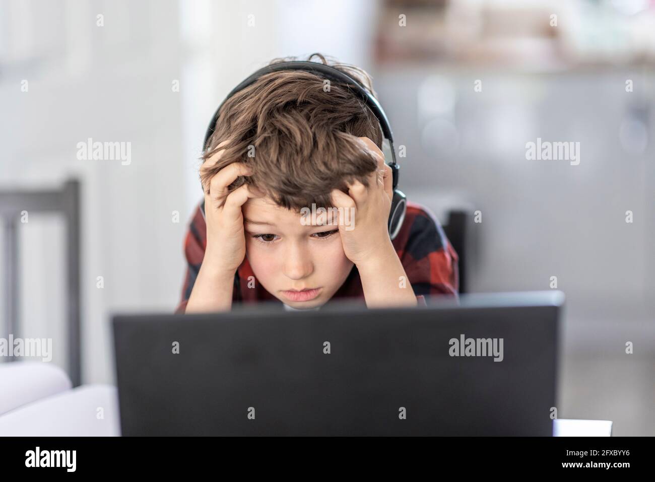 Tired boy attending remote classes through laptop at home Stock Photo