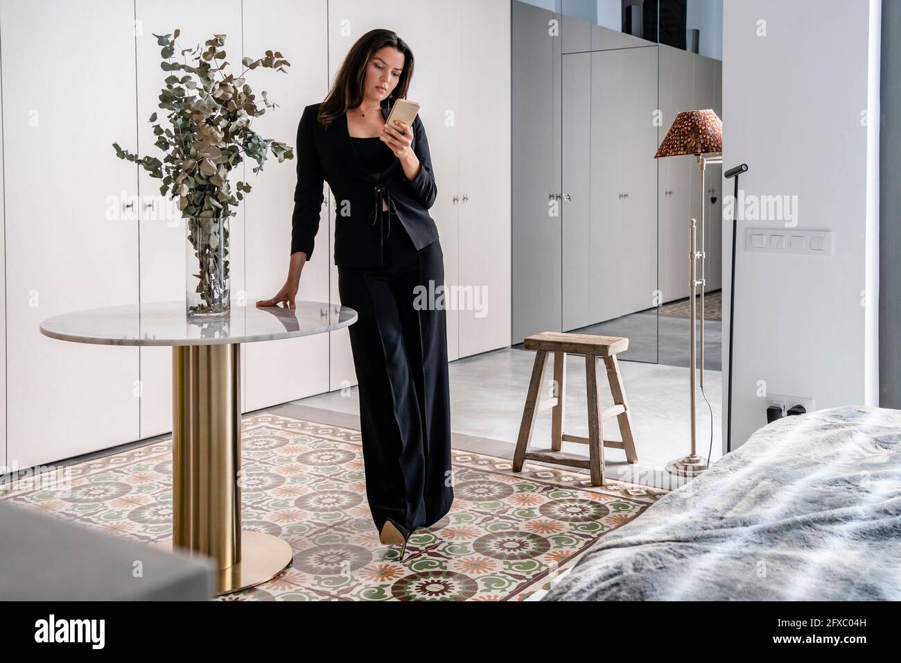 Woman using smart phone while standing at home Stock Photo