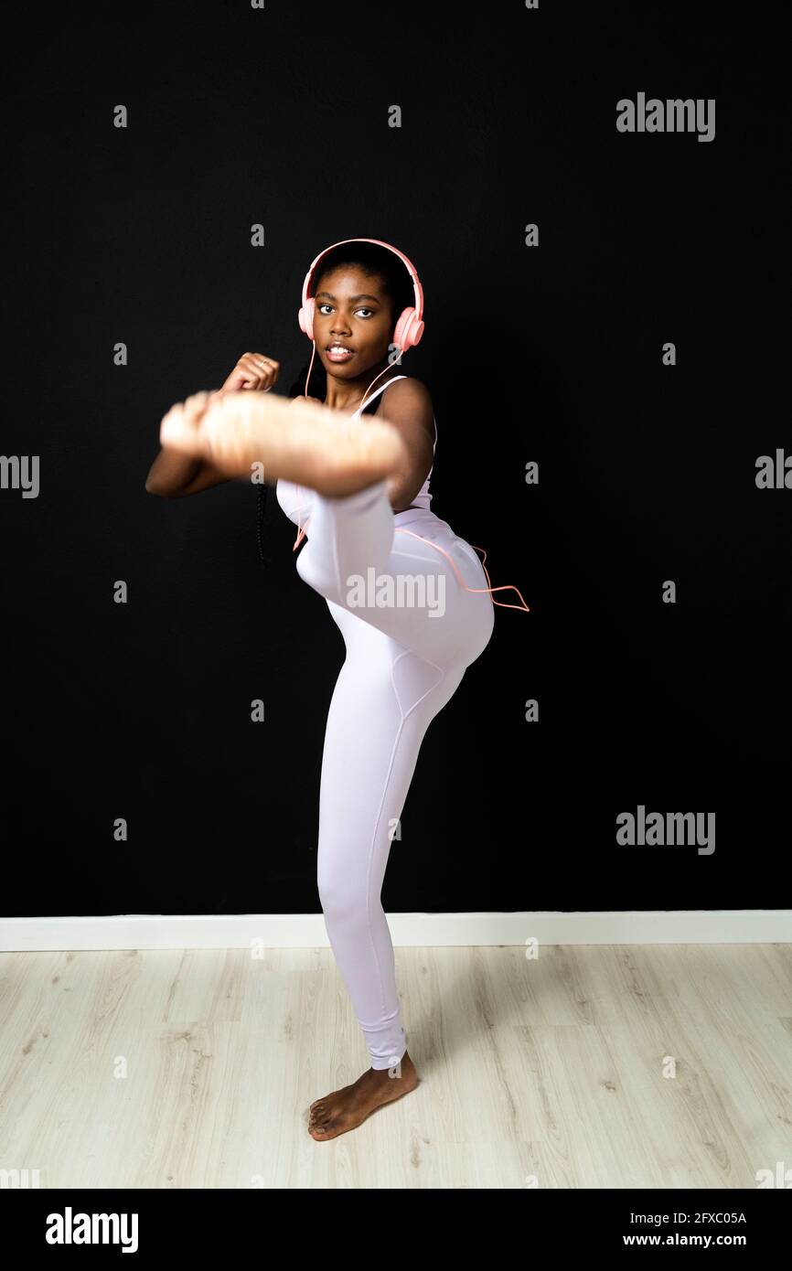 Young woman in sports clothing kicking against black wall Stock Photo