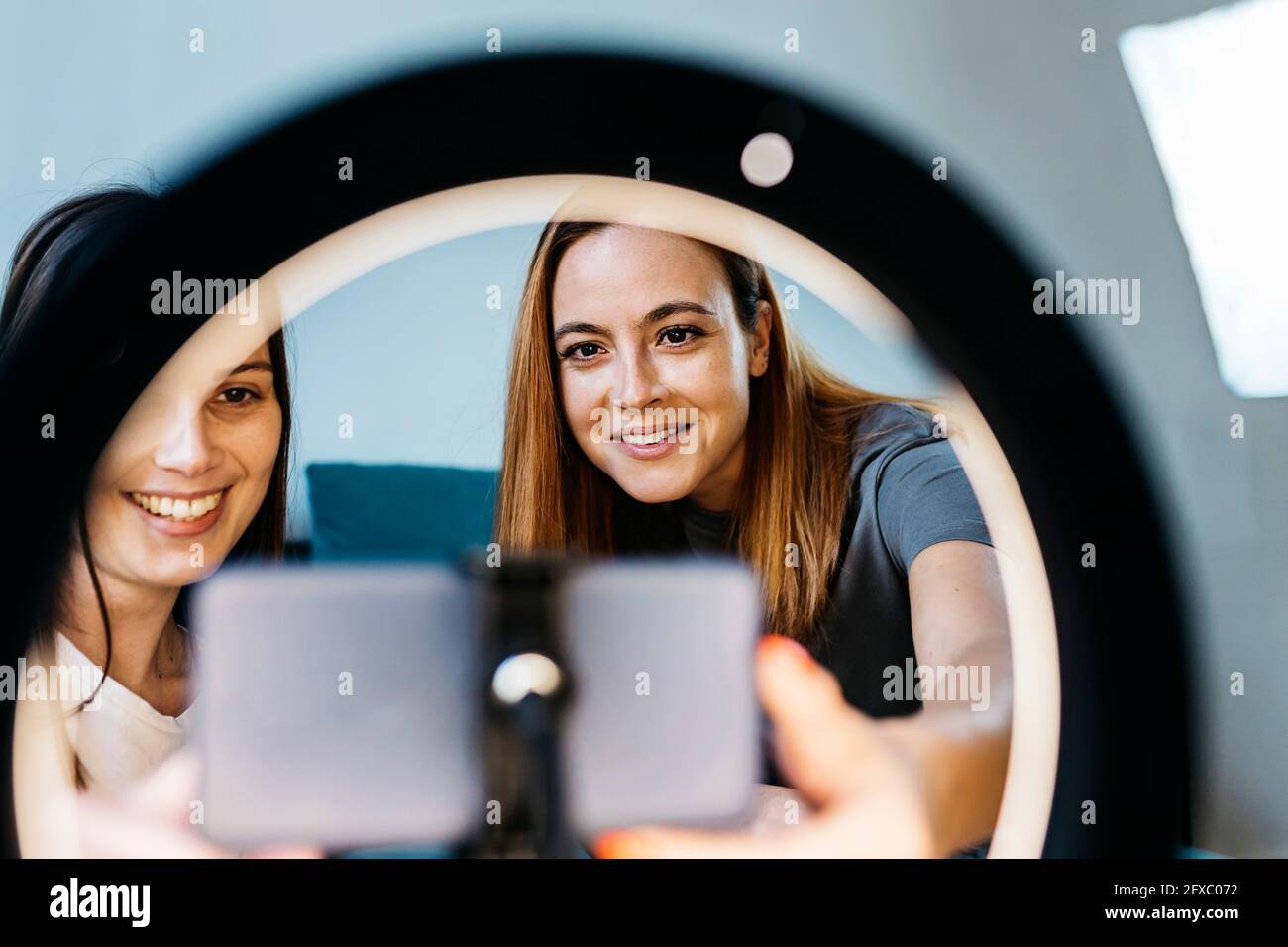 Smiling female influencers vlogging using mobile phone at home Stock Photo