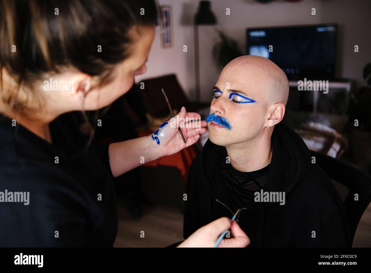 Female artist doing makeup of bald man in studio Stock Photo