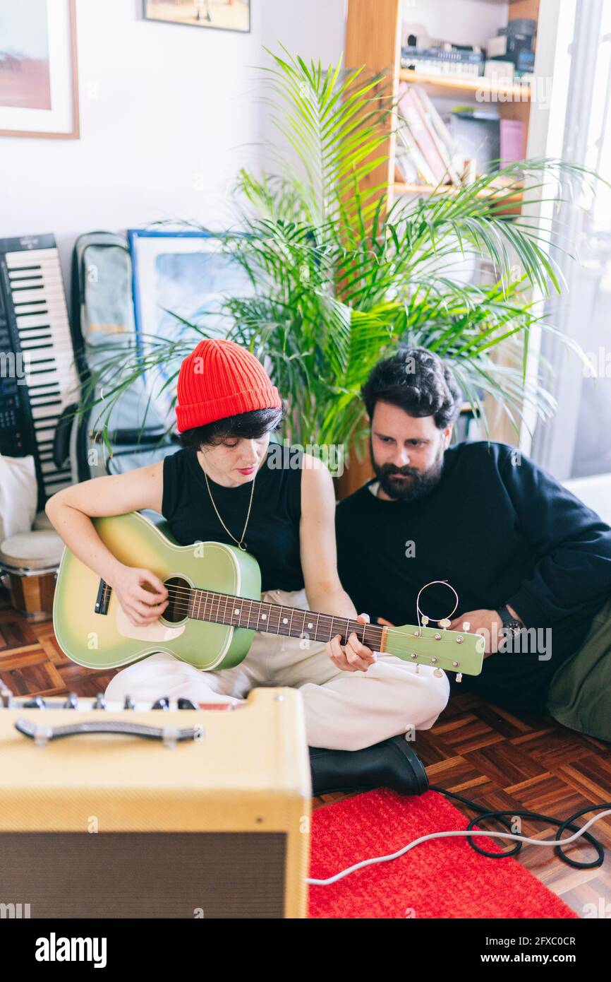 Female guitarist playing guitar while sitting by male composer in studio Stock Photo