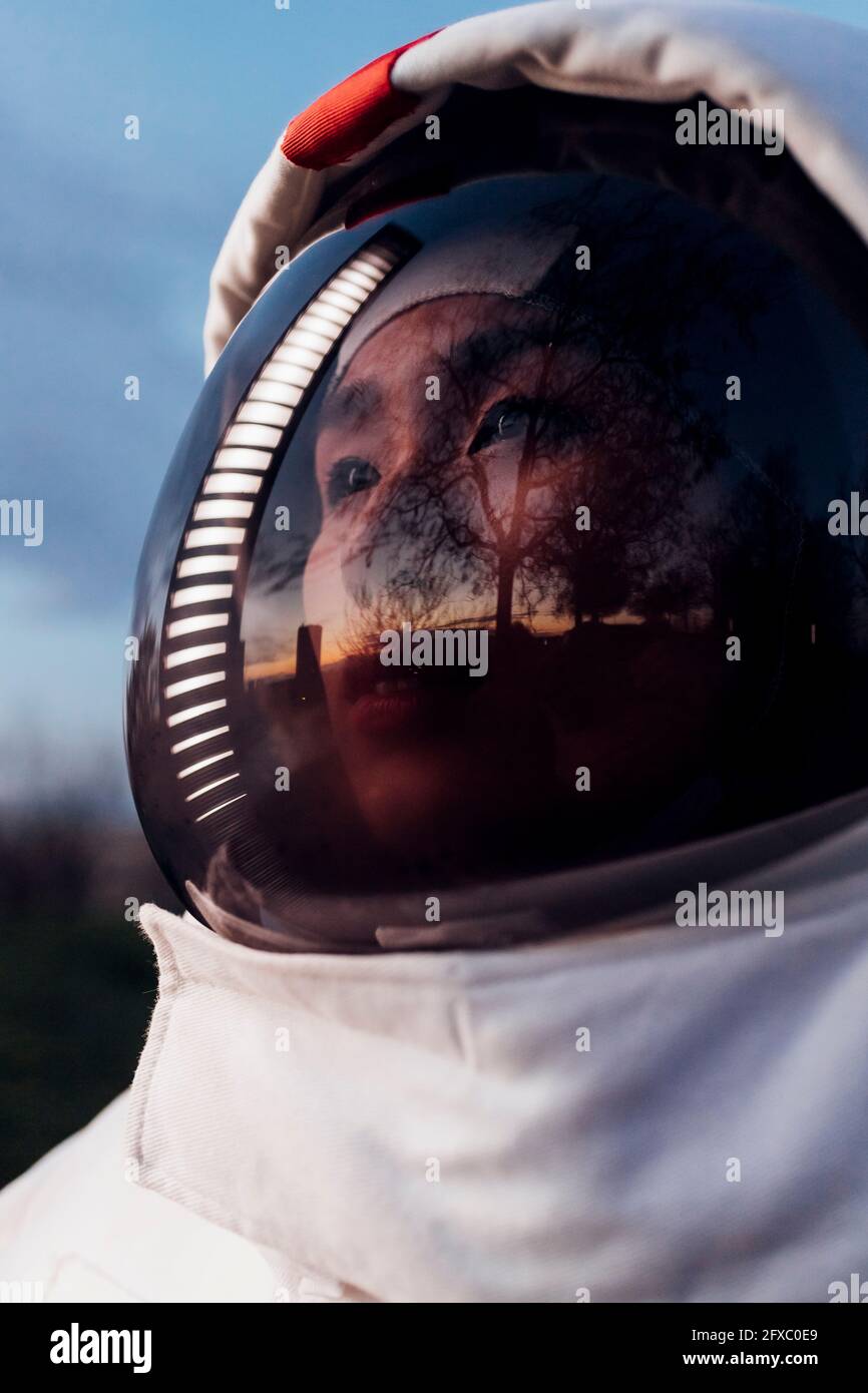 Female astronaut looking away with reflection of illuminated light on helmet during sunset Stock Photo