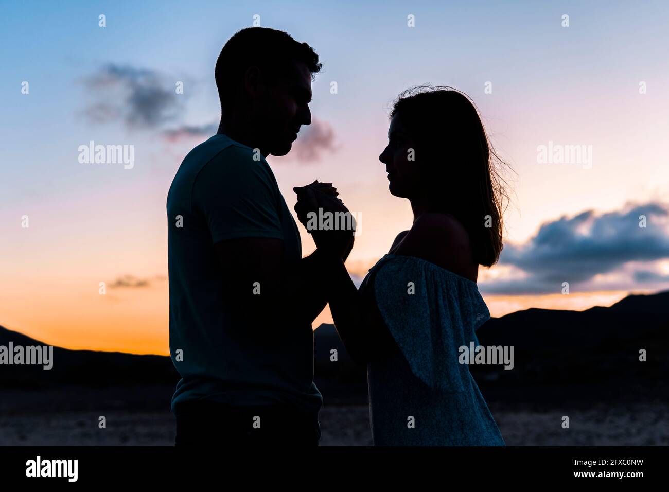 Couple holding hands while standing outdoors during sunset Stock Photo