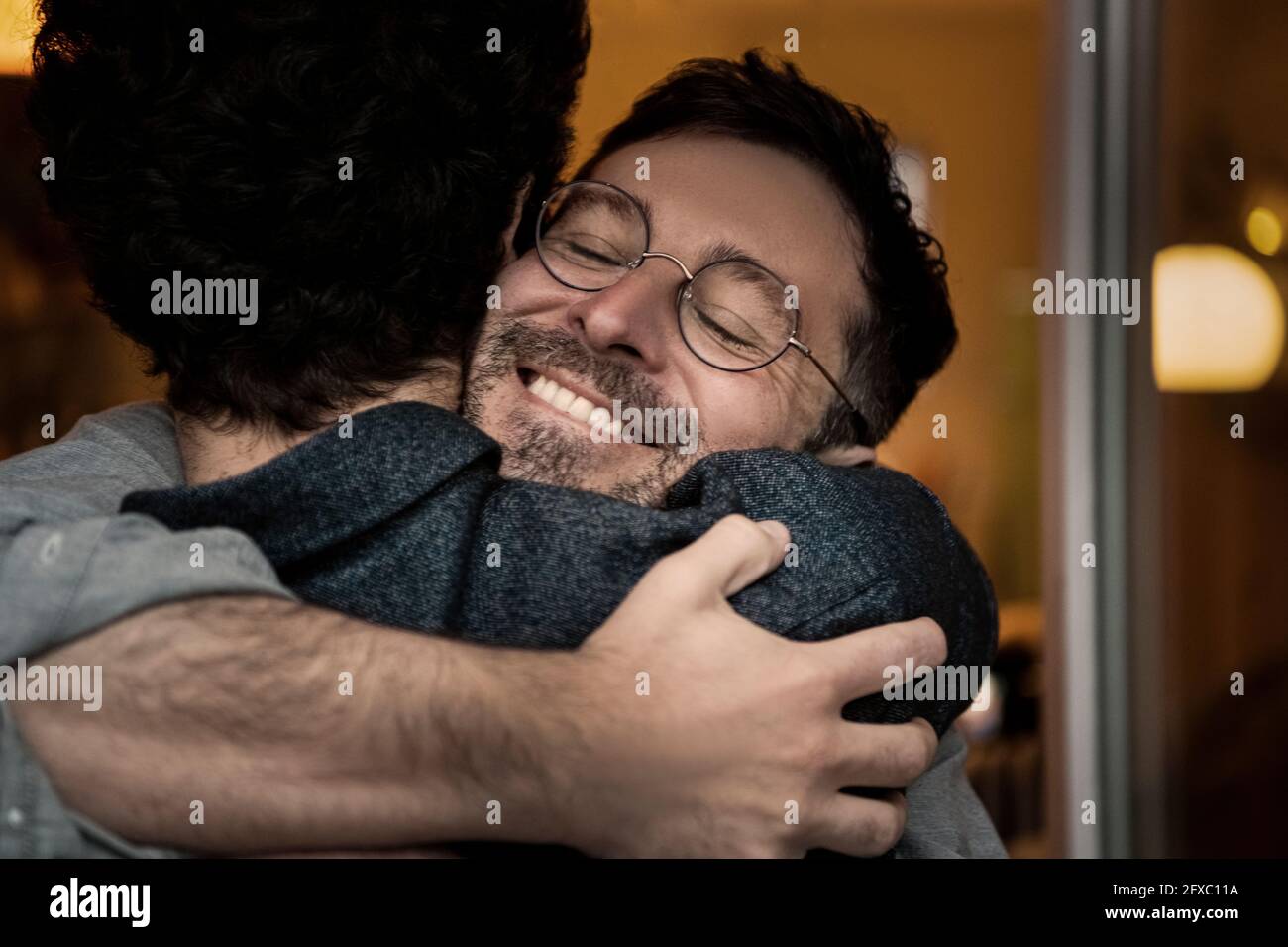Smiling mature man embracing male friend at home Stock Photo