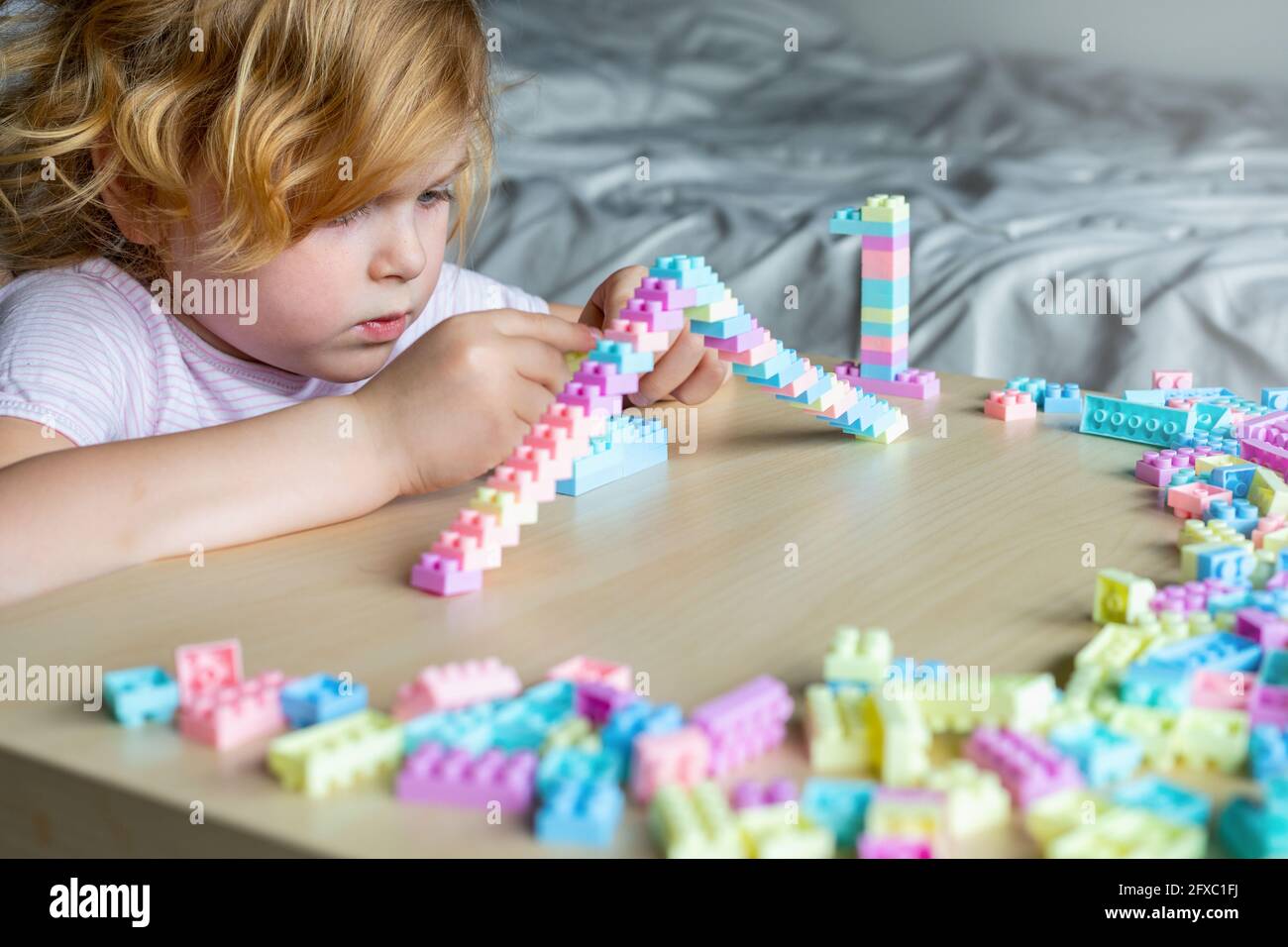 Little beautiful child playing with toy plastic building blocks, sitting at the table. Small girl busy with fun creative leisure activity. Development Stock Photo