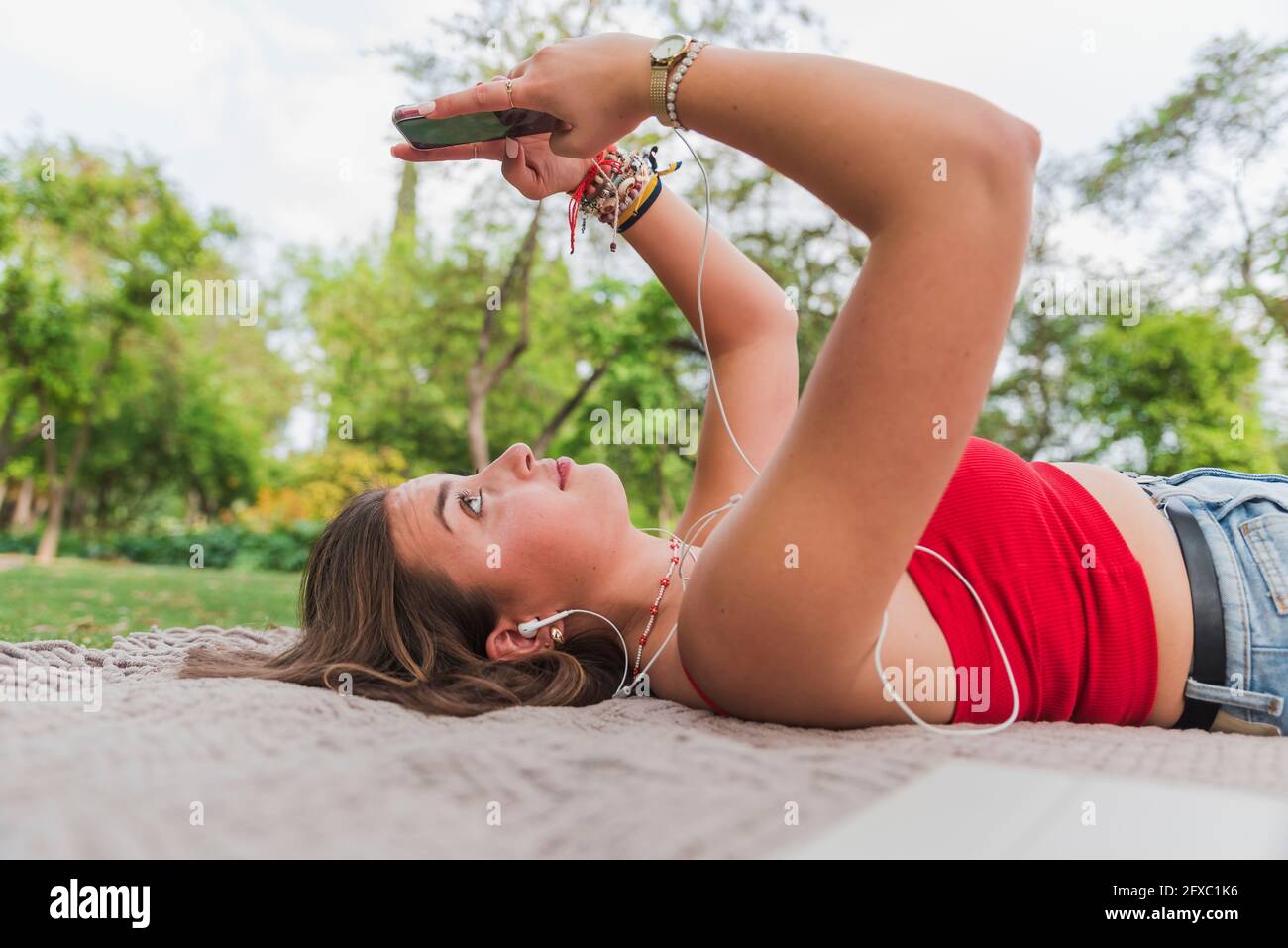 Young woman using mobile phone lying on back in park Stock Photo