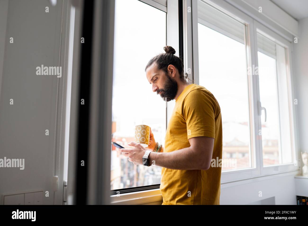 Handsome man using smart phone while standing near window at home Stock Photo