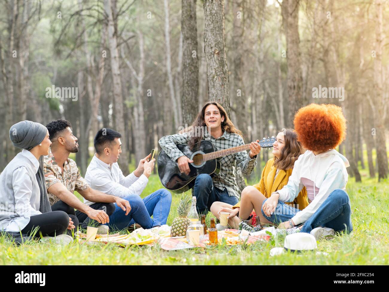 Man with male and female friends playing guitar on picnic at forest Stock Photo
