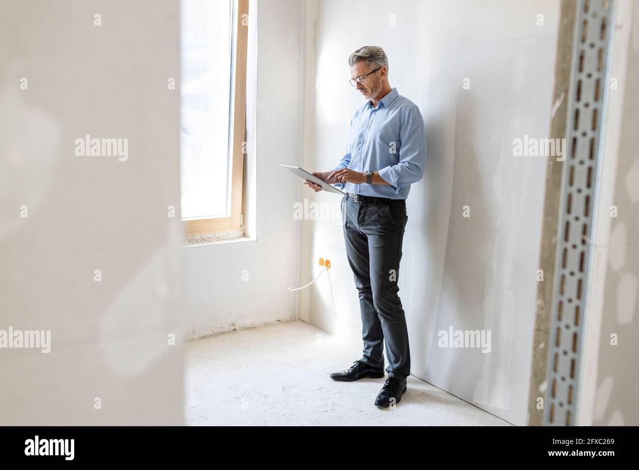Male entrepreneur using digital tablet while standing by wall at construction site Stock Photo