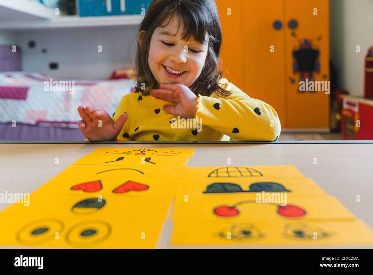 Happy girl arranging emoticons on table in playroom at home Stock Photo