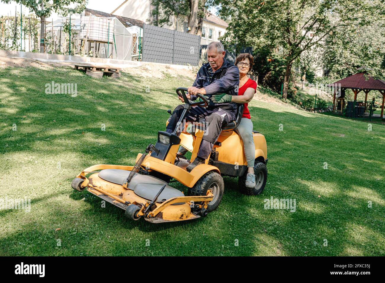 Senior couple sitting on lawn mower in backyard Stock Photo Alamy