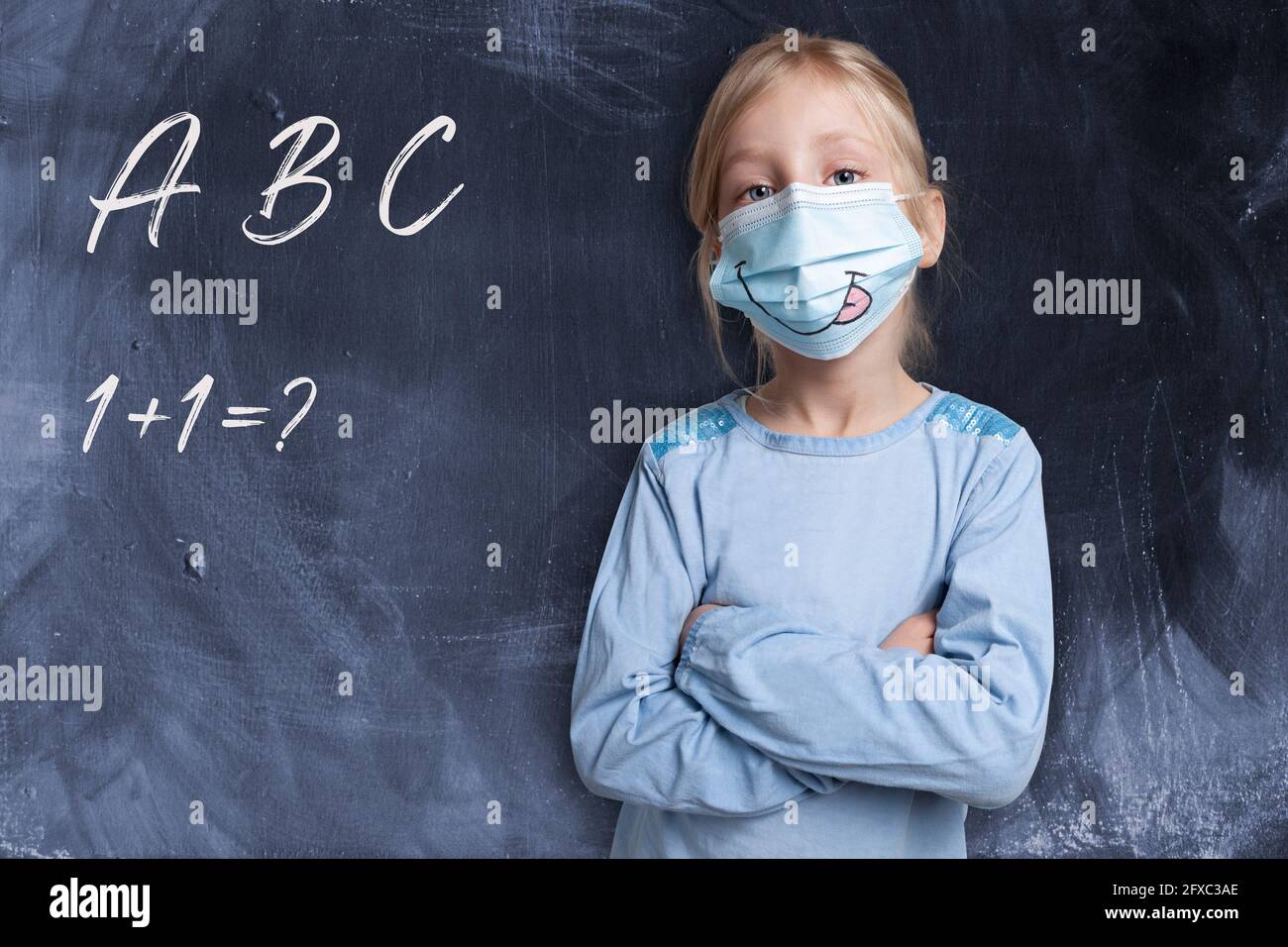 Girl with arms crossed wearing face mask by black background with alphabets and maths problem Stock Photo