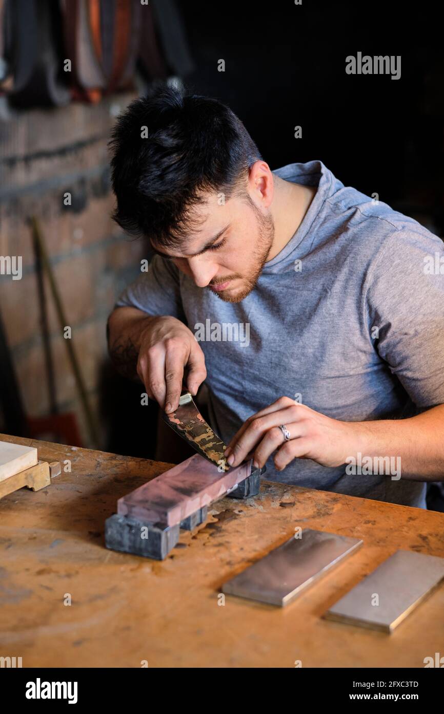 Male metal worker sharpening knife on table at workshop Stock Photo