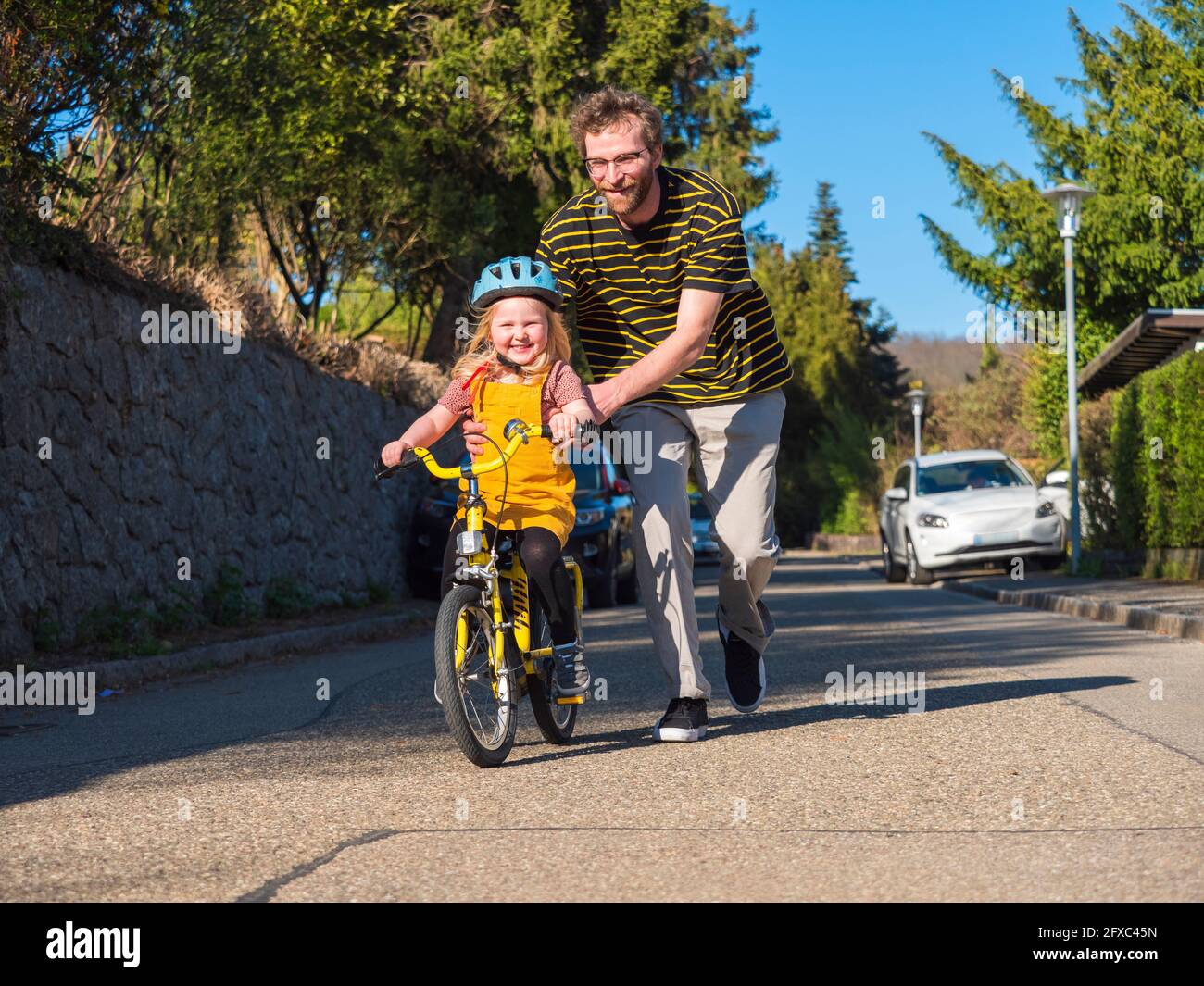 Smiling father assisting daughter while cycling on road Stock Photo