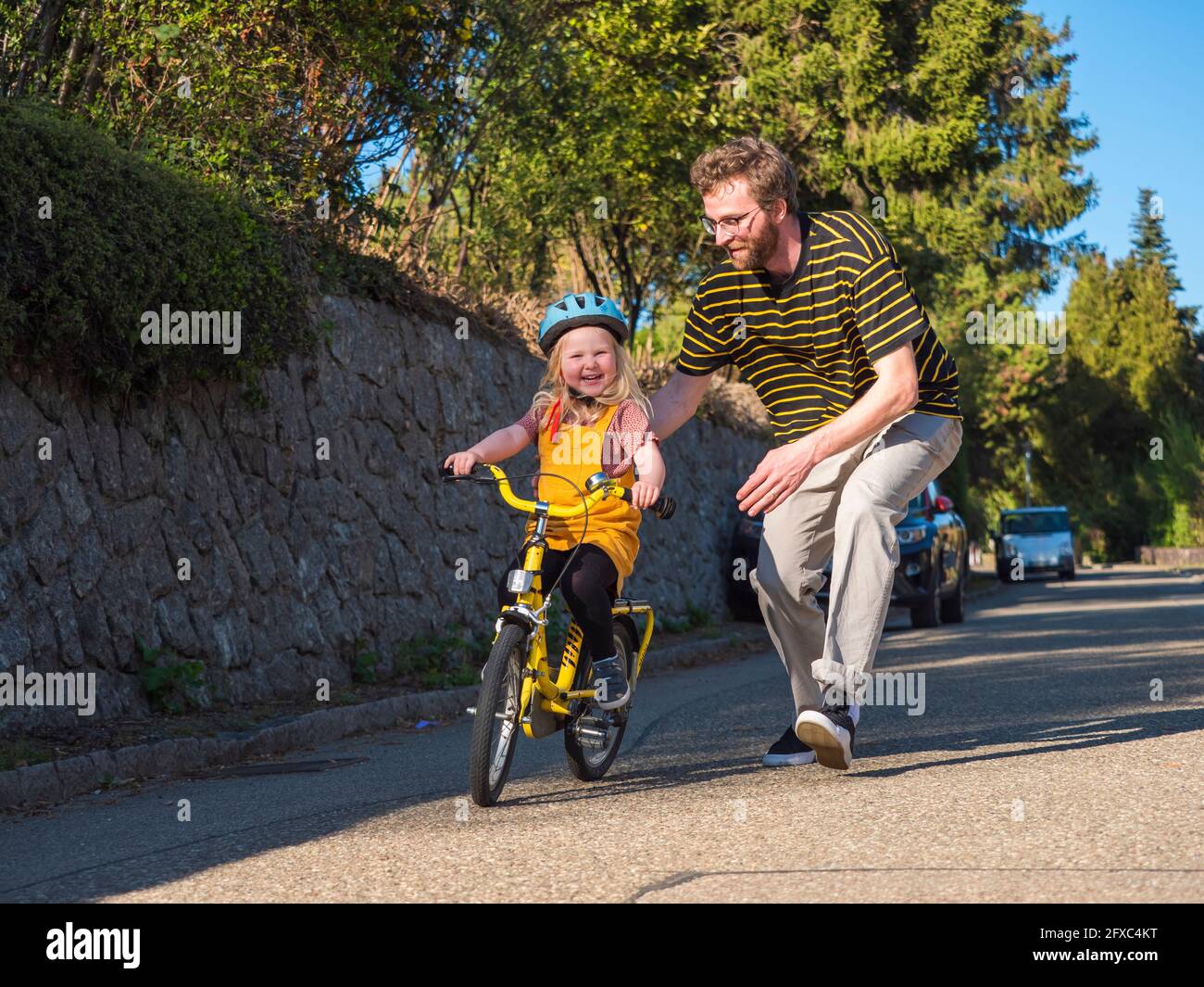 Father supporting daughter while cycling on road Stock Photo