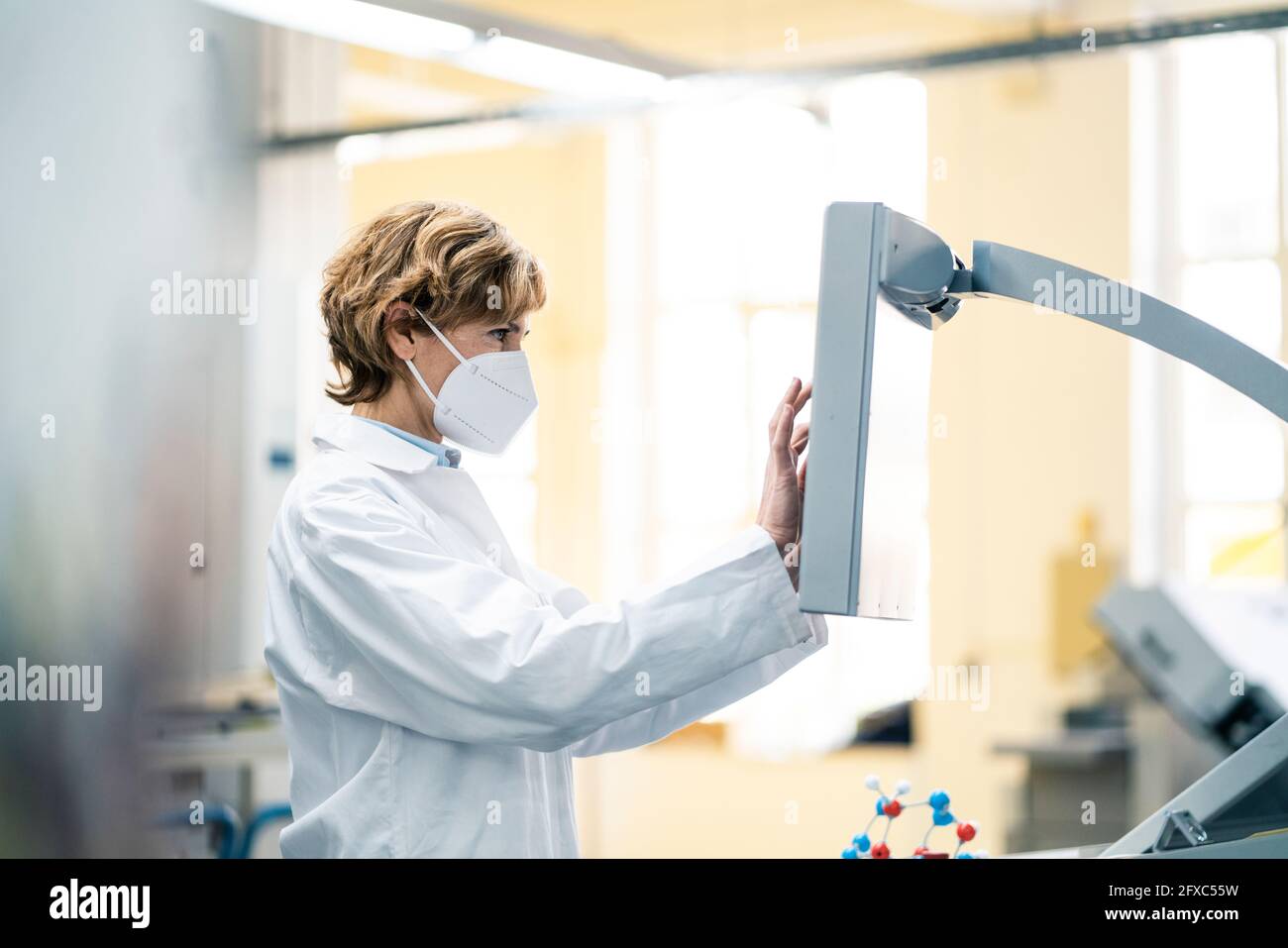 Female scientist with protective face mask using machine in laboratory Stock Photo