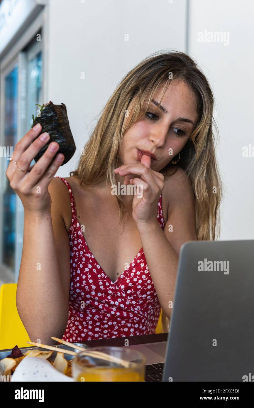 Woman licking thumb while eating food at restaurant Stock Photo