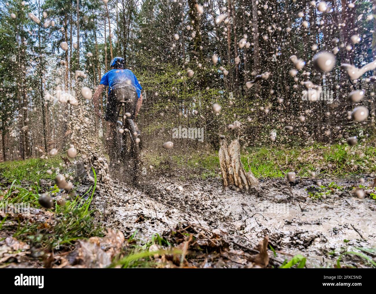 Young man riding mountain bike through mud in forest Stock Photo