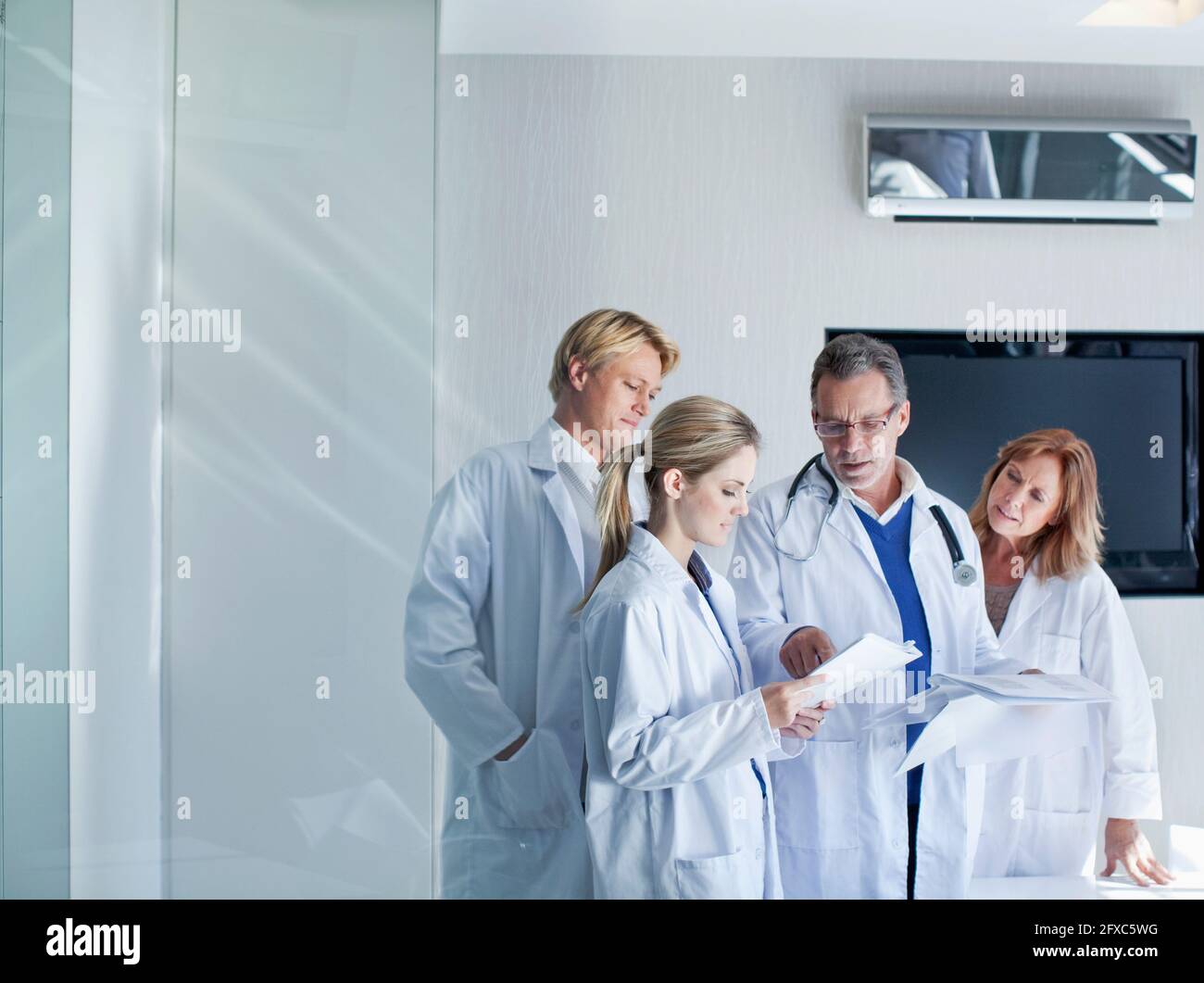 Senior doctor explaining reports to male and female healthcare workers in hospital Stock Photo
