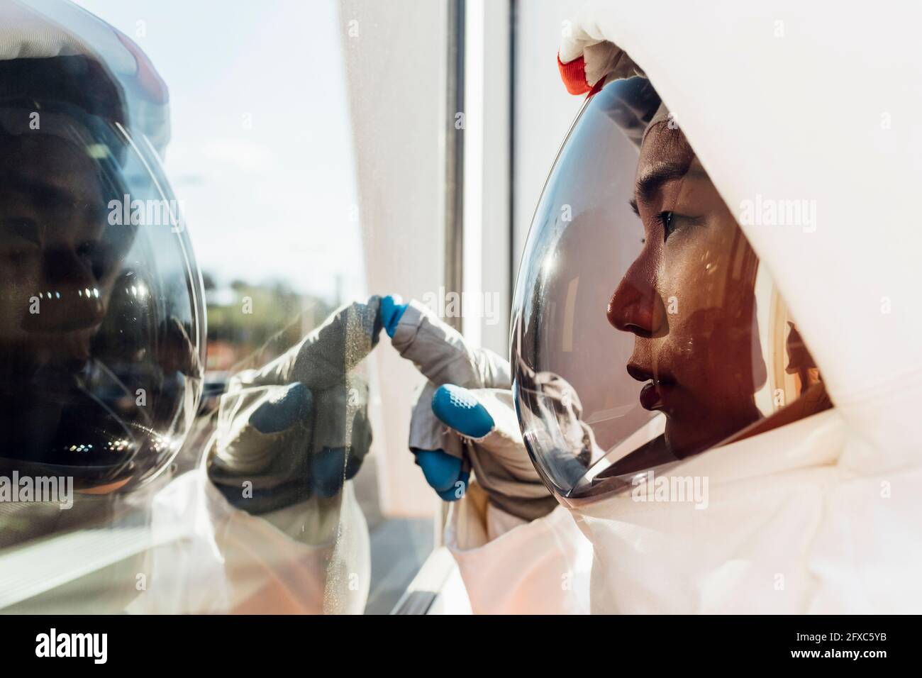 Young female astronaut in space helmet touching glass window Stock Photo