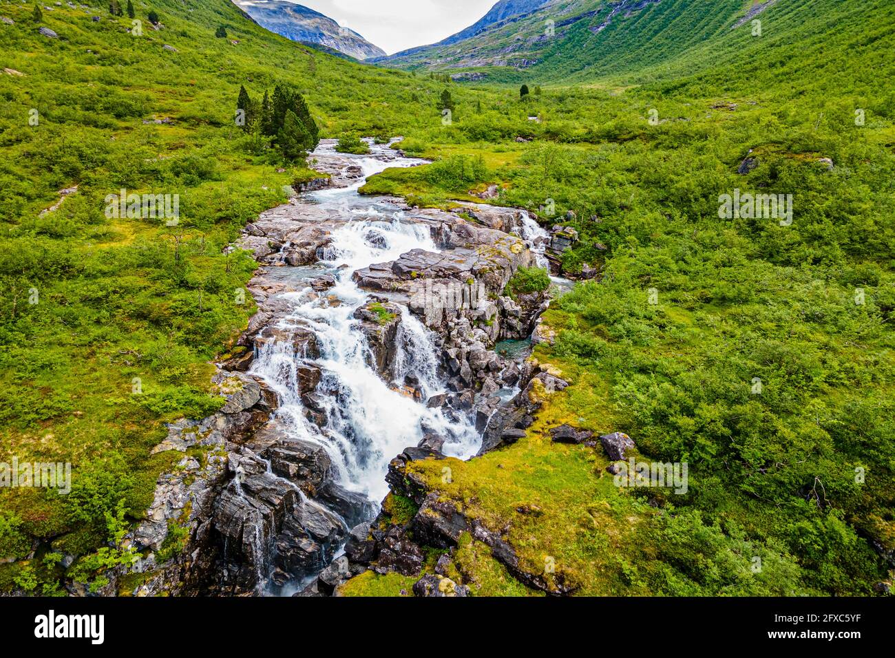 Waterfall flowing through rocks at green mountain valley Stock Photo