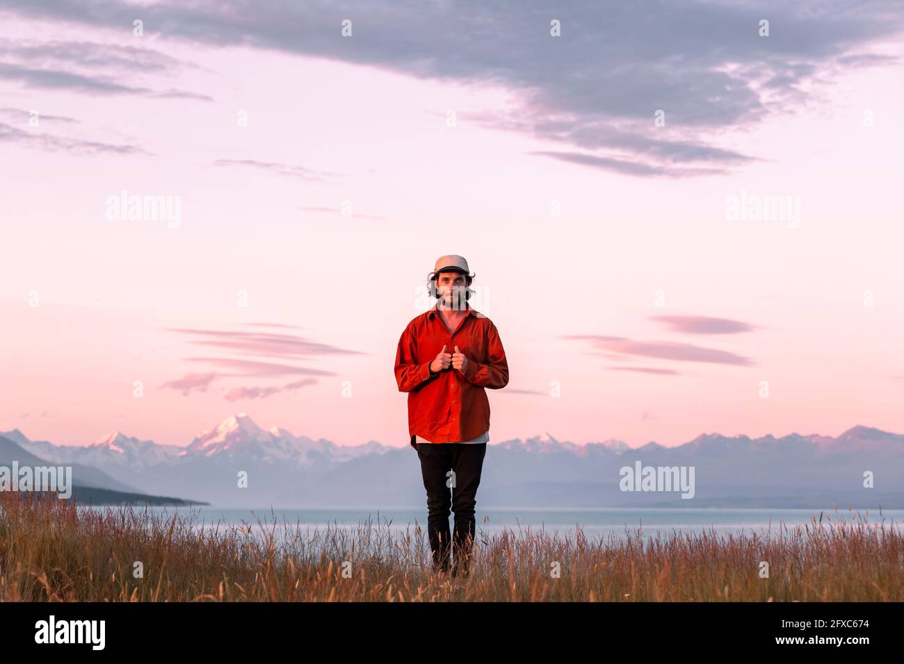 New Zealand, Canterbury, Front view of young man standing over Lake Pukaki at sunset Stock Photo
