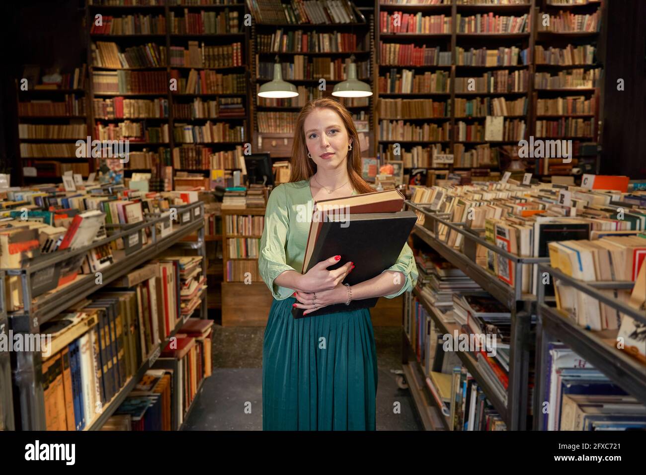 Female student holding books by shelf in library Stock Photo - Alamy
