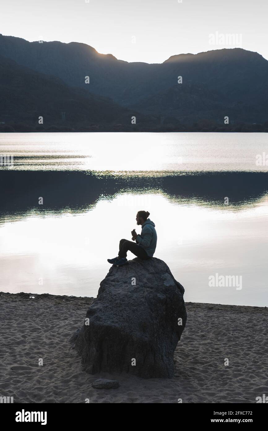 Man sitting on rock at lake during sunset Stock Photo - Alamy
