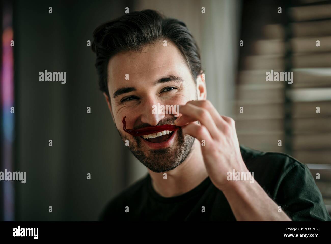 Smiling man imitating mustache with red chilli Stock Photo