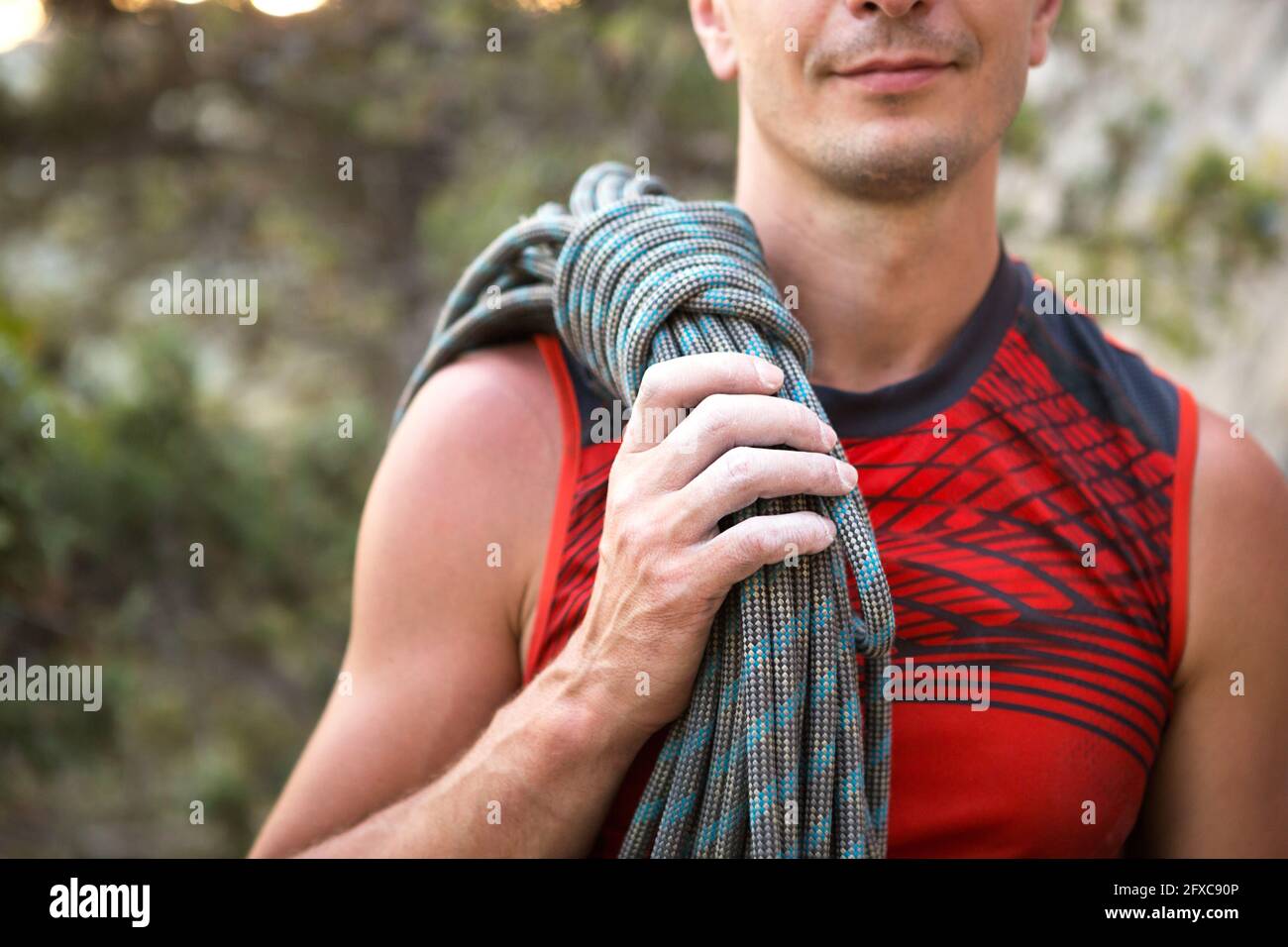A male climber of Caucasian appearance with a coiled rope in his hand ...