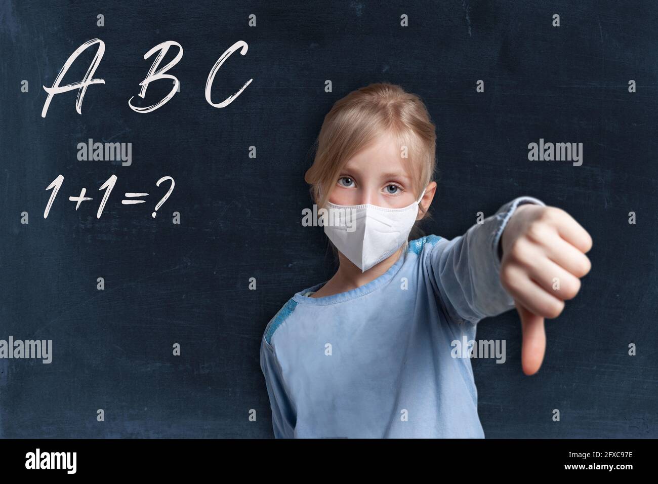 Girl showing thumbs down gesture wearing face mask against black background with alphabets and maths problem Stock Photo
