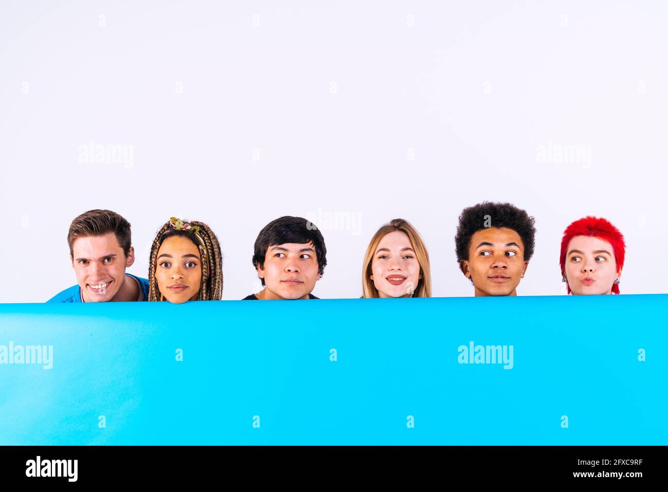 Young men and women behind blue backdrop on white background Stock Photo