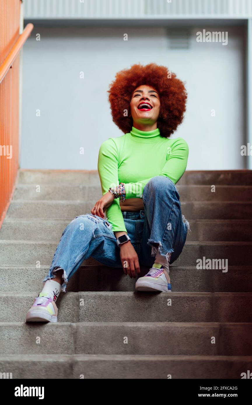 Happy woman laughing while sitting on staircase Stock Photo