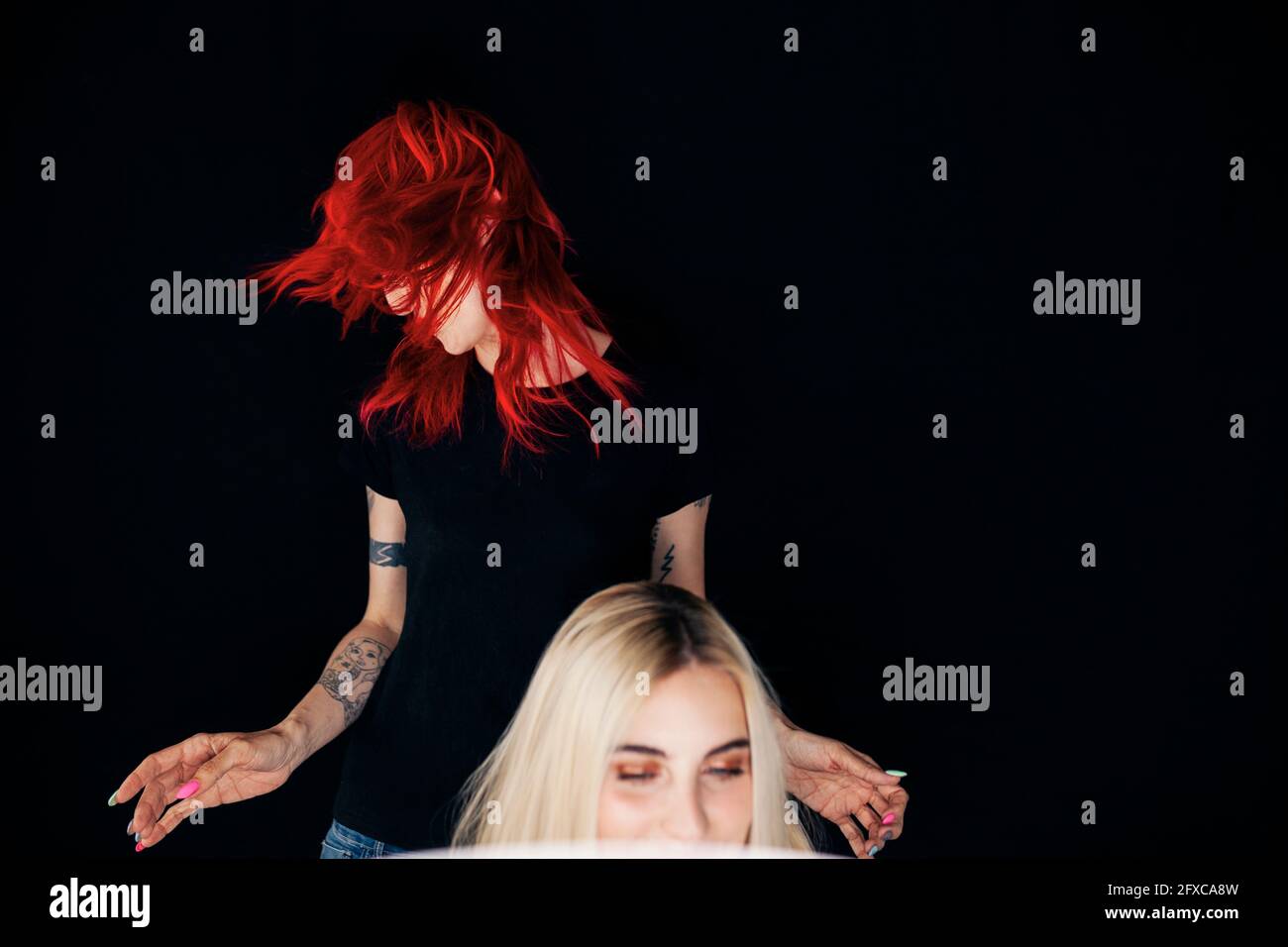 Female stylist tossing hair behind model at studio Stock Photo