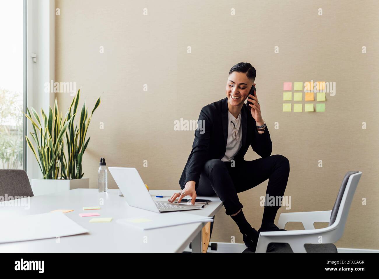 Female entrepreneur talking on mobile phone while using laptop at office Stock Photo
