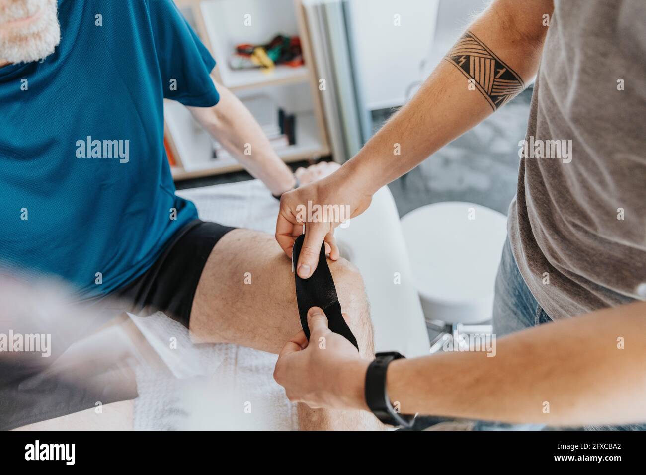 Male physiotherapist sticking elastic therapeutic tape on knee of patient Stock Photo