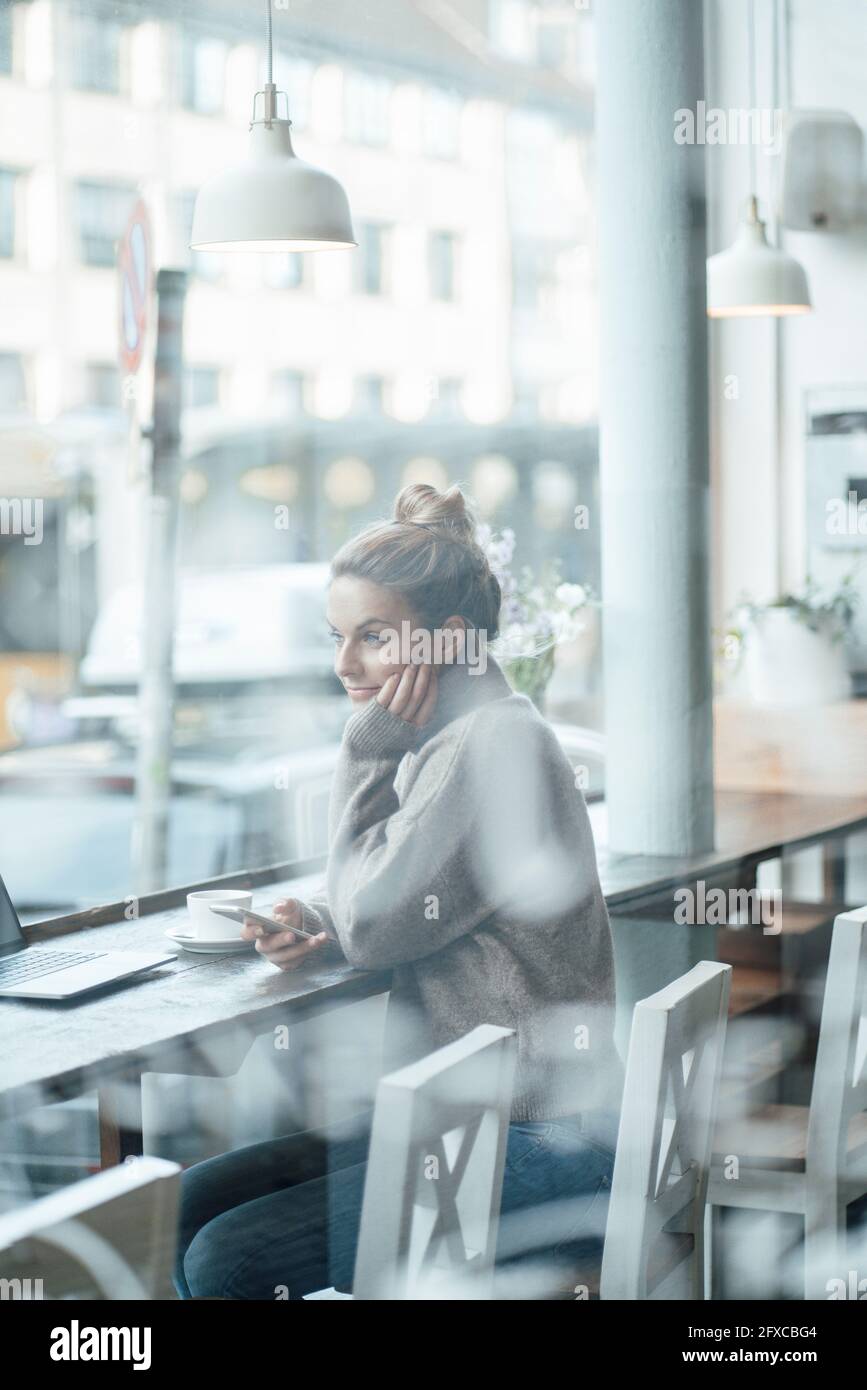 Businesswoman looking through window while sitting at coffee shop Stock