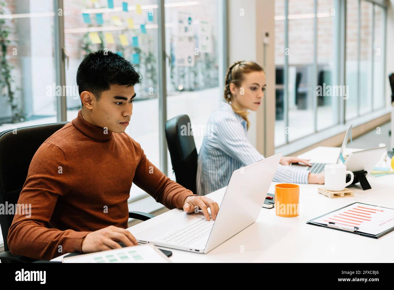 Male entrepreneur working on laptop by colleague at office Stock Photo