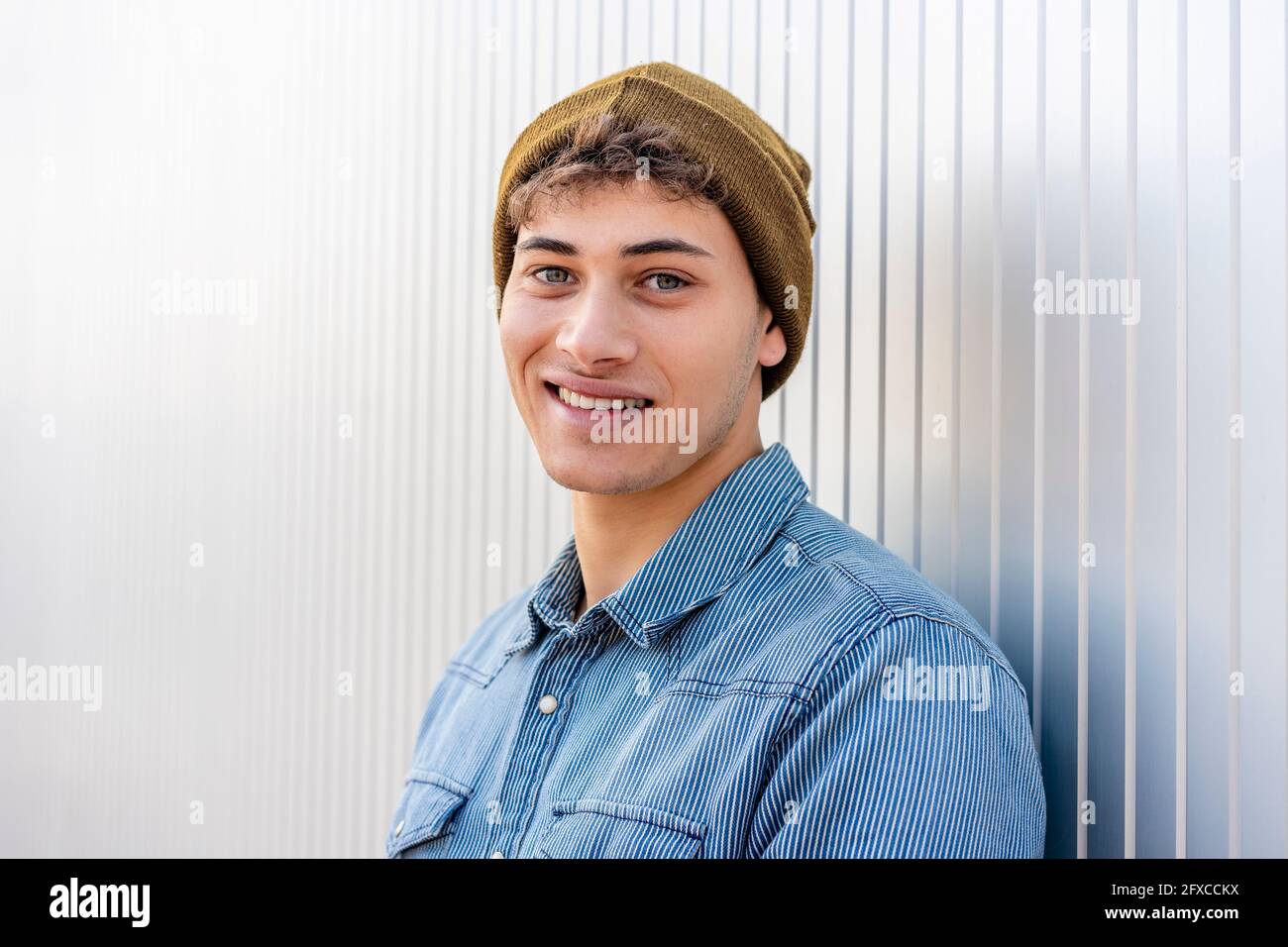 Smiling man wearing knit hat by silver colored wall Stock Photo