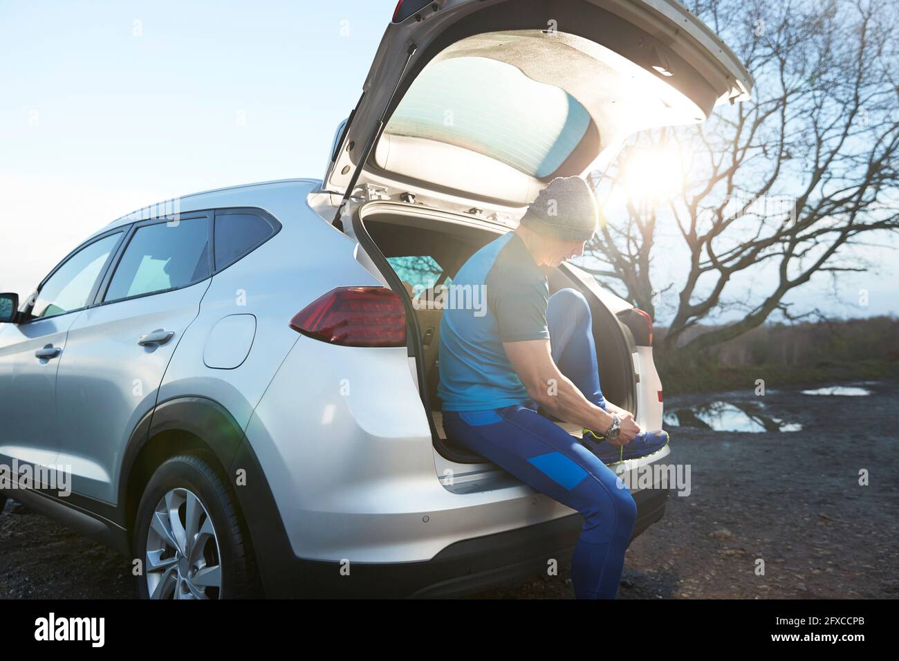 Athlete tying shoelace while sitting in car trunk Stock Photo