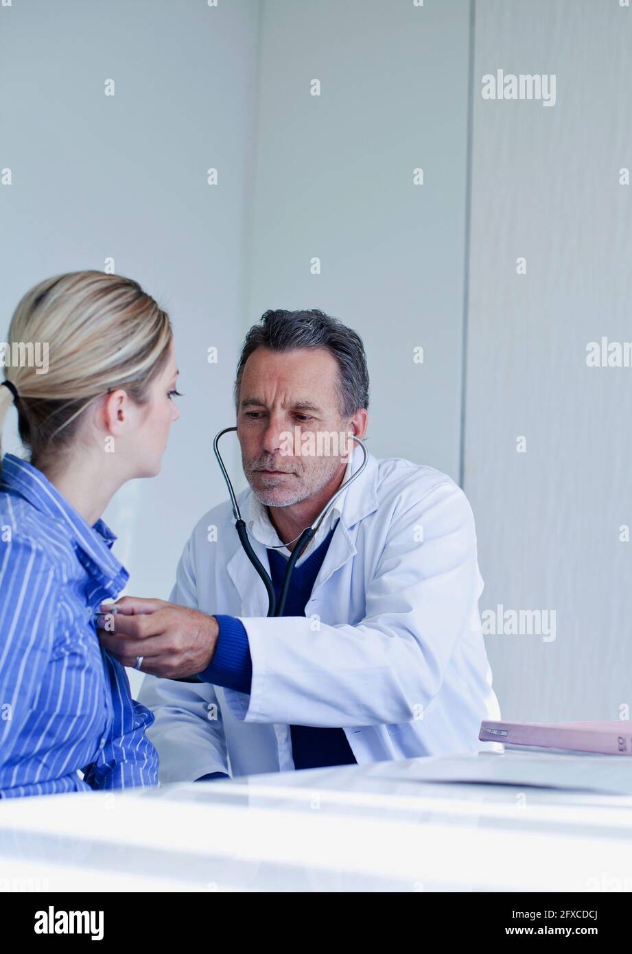 Male doctor assessing female patient with stethoscope in hospital Stock ...