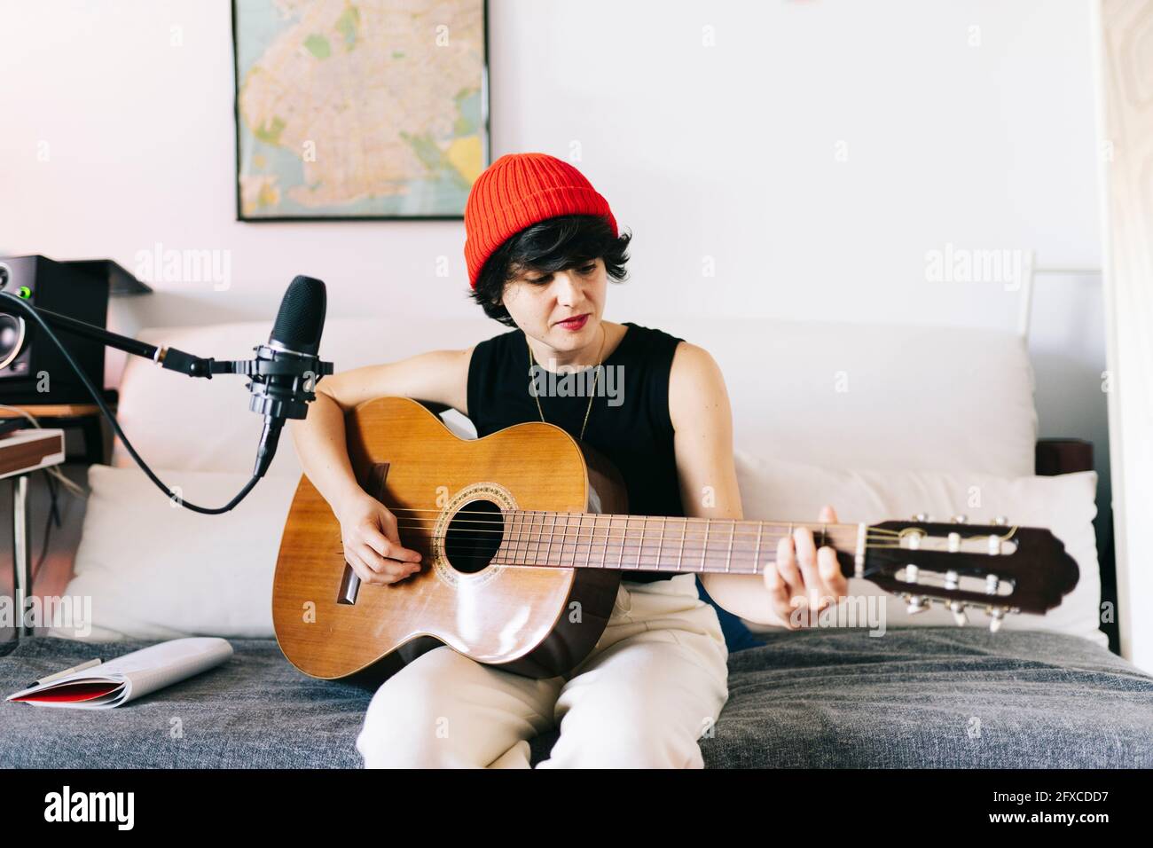 Female composer wearing knit hat playing guitar while recording at studio Stock Photo