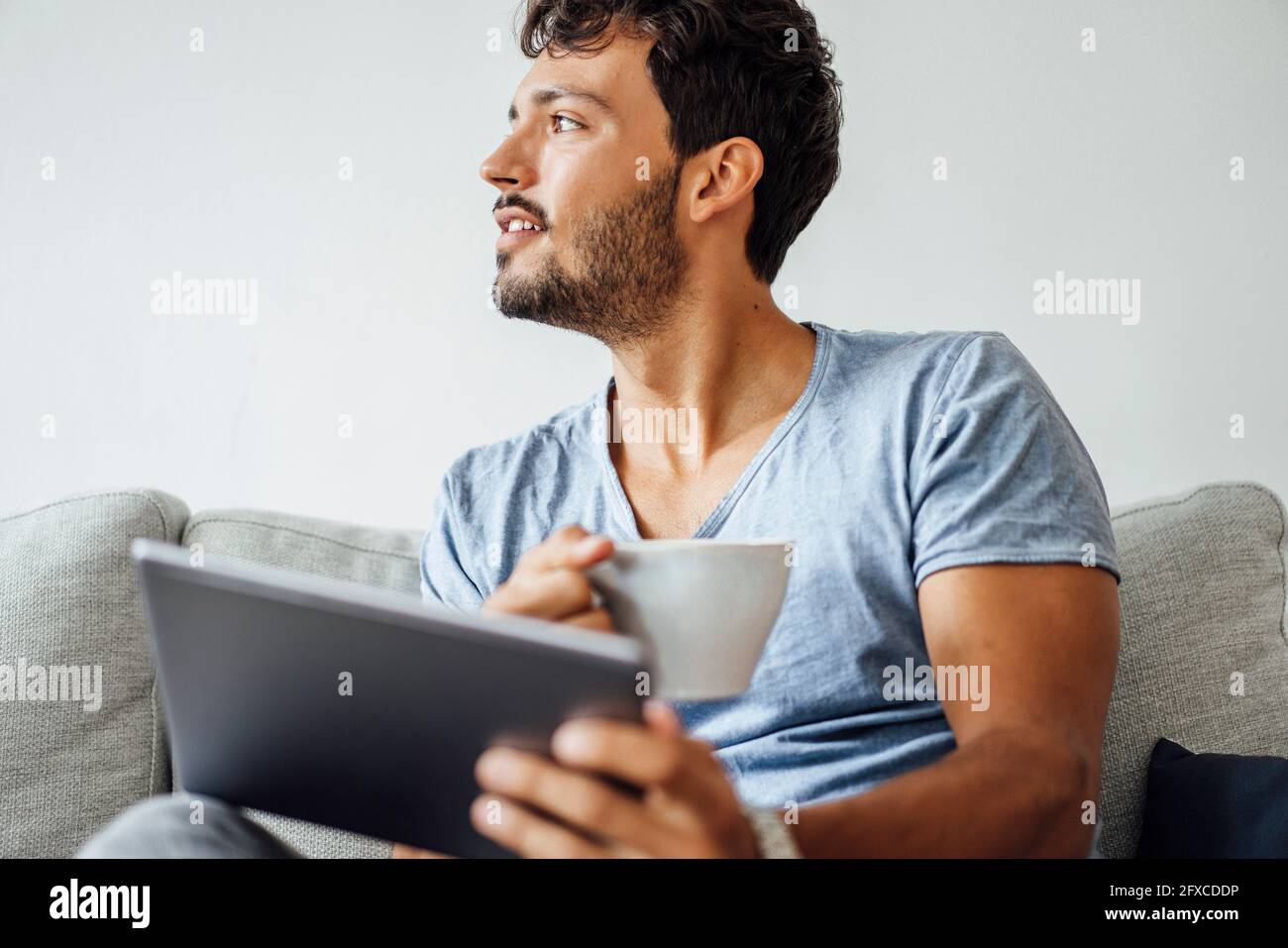 Young man sitting with coffee cup and tablet while looking away Stock Photo