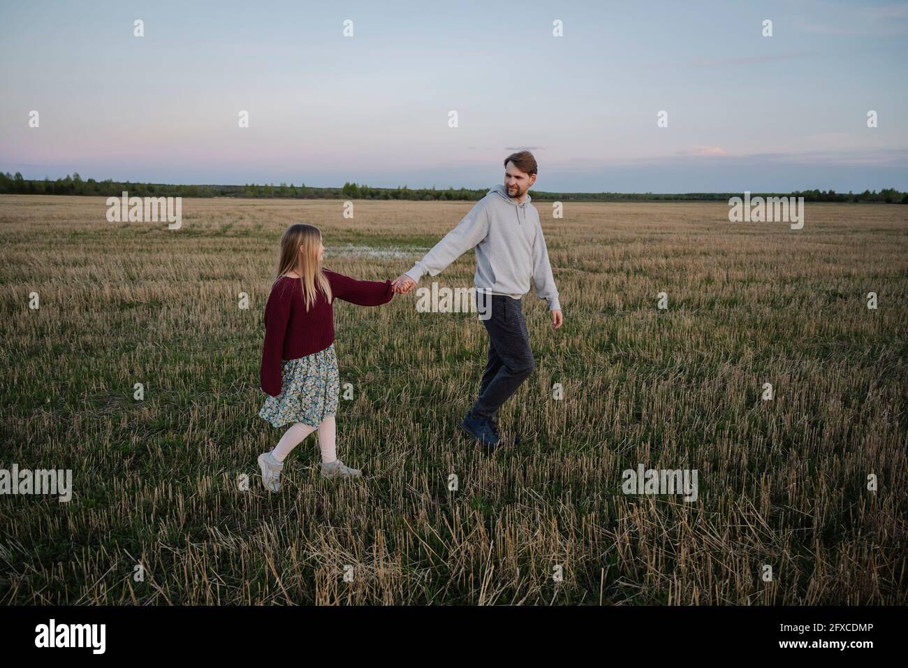 Father and daughter holding hands while walking in agricultural field Stock Photo
