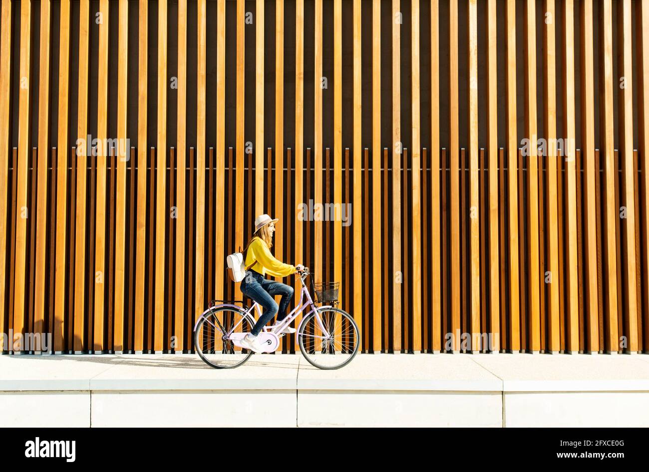 Young woman with backpack cycling bicycle on footpath Stock Photo