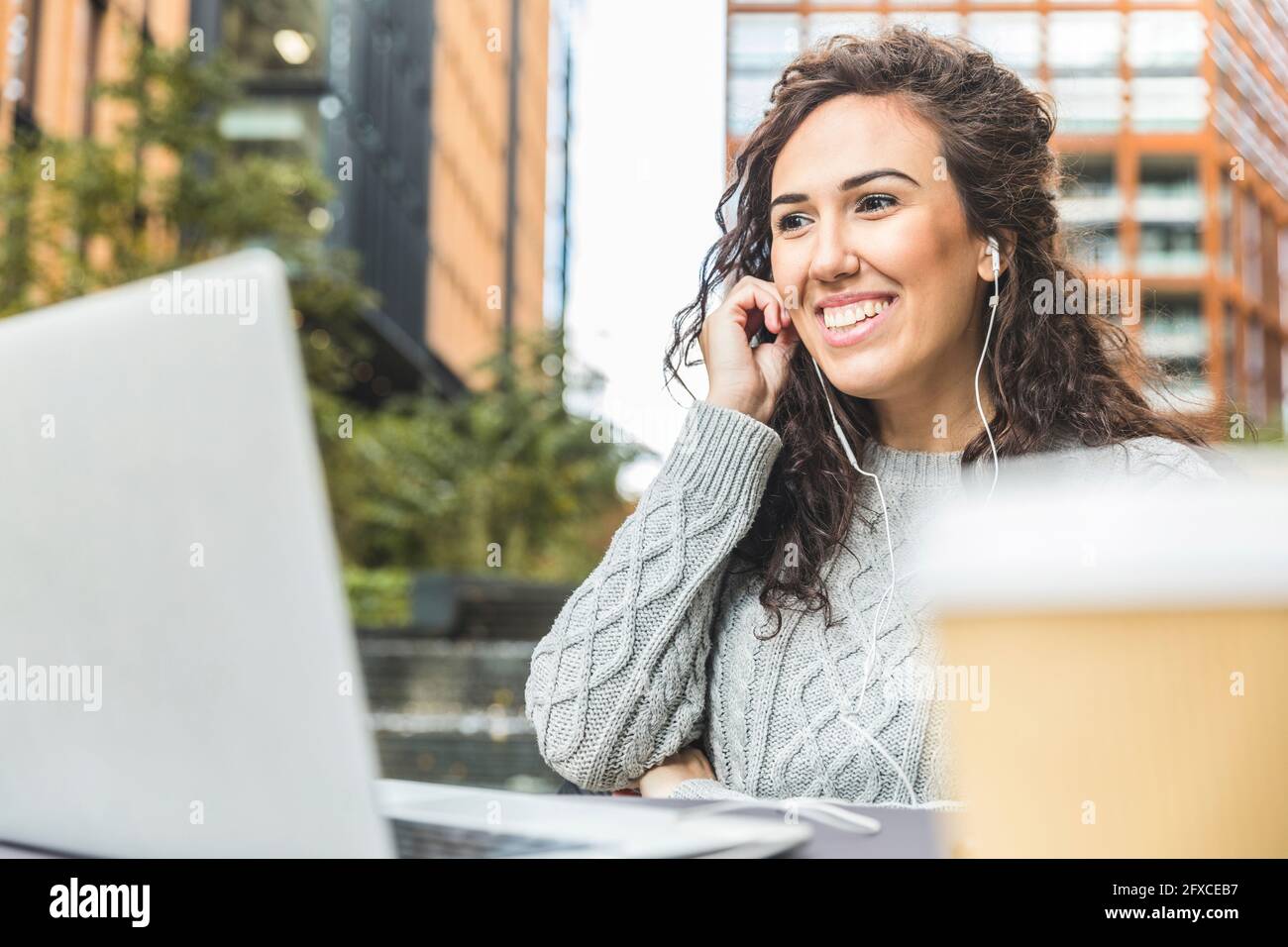 Happy businesswoman wearing headphones looking at laptop at cafe Stock Photo