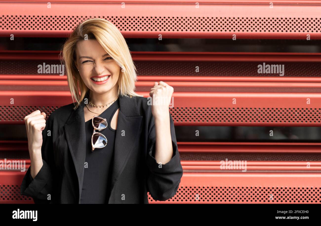 Excited woman clenching fists in front of corrugated wall Stock Photo
